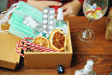 Christmas gift with antiseptics medical masks lollipops and pills on a wooden table. Dried orange slices in a box. a glass glass with vitamins and pills. new year's in quarantine.