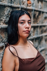 Fototapeta premium vertical portrait of an attractive and young chinese woman leaning on a wall and looking at camera