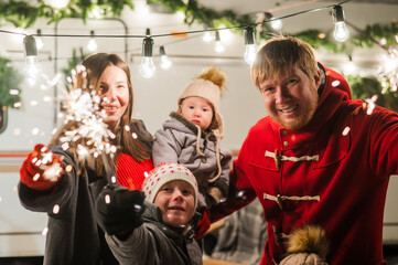Happy family celebrates christmas in nature and holds sparklers. Parents with three sons travels in a van.