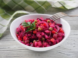 Seasonal salad vinaigrette with beetroot in a white bowl,   napkin, fork on a white wooden table. Healthy food with vegetables for vegetarian dietary nutrition, closeup