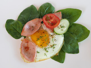 Isolated fried eggs with fried sausage with spinach leaves, tomato and cucumber slices on a white background. Delicious appetizer with chicken egg, wurst products and vegetables for breakfast