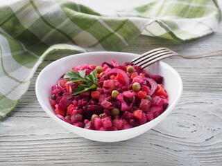 Seasonal salad vinaigrette with beetroot in a white bowl,   napkin, fork on a white wooden table. Healthy food with vegetables for vegetarian dietary nutrition, closeup