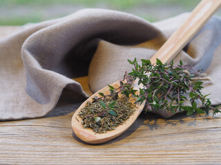Dry herb in a wooden spoon and twigs of thymus grass with a napkin on a wooden table, closeup....