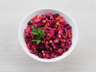 Seasonal salad vinaigrette with beetroot in a white bowl, napkin on a white,  top view, flat layout. Healthy food with vegetables for vegetarian dietary nutrition, closeup