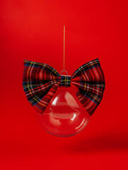 Christmas tree bauble ornament with bow-tie flying on vibrant red background. Creative New Year and Xmas party festive concept. Winter holiday season decoration. Greeting card with empty copy space.