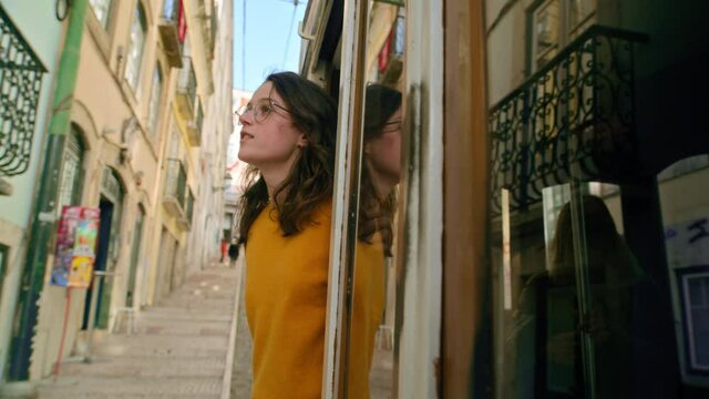 Beautiful and authentic millennial young woman lean out of window of old tram in Lisbon, Portugal city centre. Concept amazing european summer vacation, wanderlust trip in cinematic urban destination