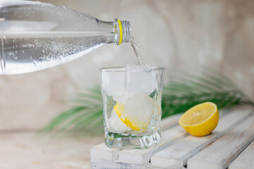 water or tonic is poured from a bottle into a glass with ice and lemon - obrazy, fototapety, plakaty