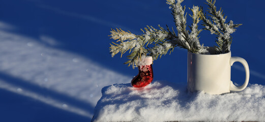 Snow-covered branch of a Christmas tree decorated with toys in white cup on snow background. Concept of Holiday Christmas and New Year outdoors. Close-up with copy space.