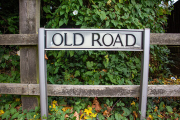 Old Road street name sign on two posts with an old wooden fence and ivy in the background