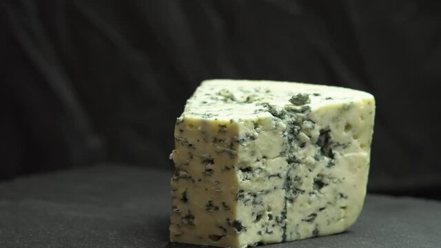 Knife cuts blue noble blue cheese is spinning on a plate. Texture of blue cheese. Fragrant blue cheeses with noble mold