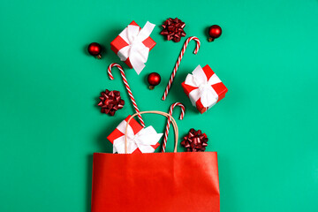 Red paper shopping bag with Christmas decorations and gift on green background with copy space for...