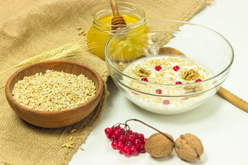 Cereal uncooked flakes in wooden bowl on sackcloth. Barley flake porridge with milk, honey, guelder rose and walnuts. Healthy, organic food. Traditional recipe