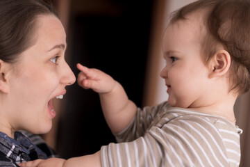 Portrait Adorable Face Of Little Cheerful Happy Toddler Daughter baby Charming Smile Look At Mom Strong Cuddles Loving Mommy Together. child catches holding mom by nose sincere feelings love care