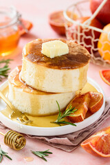Fluffy Japanese Soufflé pancakes with honey and red oranges on a white plate. Pink background....