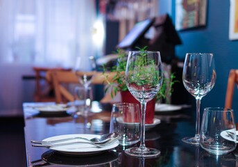 clean crystal wine glasses and cutlery on black table	with flowerpot in empty restaurant