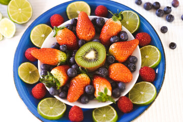 Close-up on a blue plate full of strawberries and blueberries with half a kiwi. Concept of healthy nutrition and diet