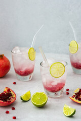 Refreshing pomegranate drink in glasses with pomegranate seeds and ice, lime and glass straws, cut pomegranates with seeds