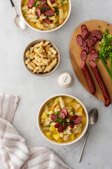 Potato and yellow pea soup with croutons and smoked meats in bowls, cutting board with chopped green onions and smoked sausage, top view