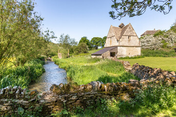 The old stone dovecote (c.1600 AD) beside the infant River Windrush as it flows through the...
