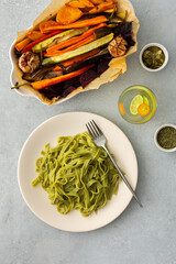 Green pasta tagliatelle with baked vegetables and pumpkin seeds and a glass with water and citrus, top view