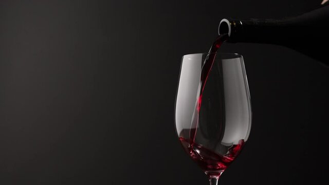 Slow motion pour red wine into wineglass on black background