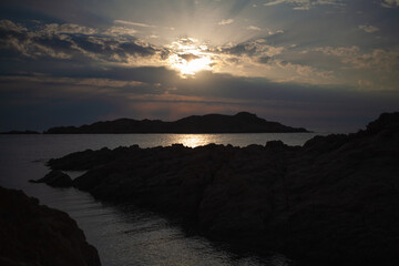 Aerial shot of a rocky shoreline and tranquil seawater beautiful shining in the sun. Drone flying between rock formations.