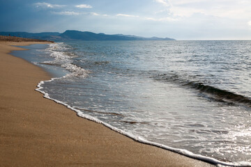 Low angle shot of the sandy beach, with footprints and seaweed, lapped by waves in fast motion.