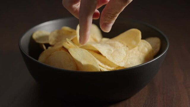 Slow motion man hand take potato chips from black bowl on wood table