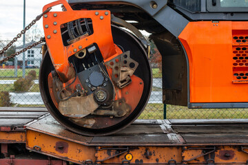 Details of an orange road roller standing on a transport trailer