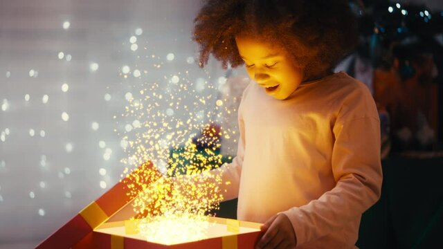 Little Girl Opening Box With Christmas Present, Gift Shining With Magic Light. Cozy Christmas Night Atmosphere