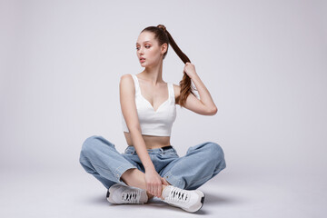High fashion photo of a beautiful elegant young woman in a pretty white top and sneakers, blue...