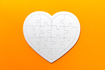 Obraz na płótnie Canvas Puzzle pieces on orange background. White heart puzzle pieces grid. Healthcare concept. Copy space for text, top view, close up.