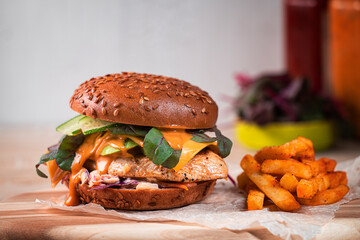 Close-up homemade burger with chicken breast, vegetables and fries. Burger with sesame bun, fried chicken breast, one melty slices of cheese, avocado, salad, cucumbers, coleslaw