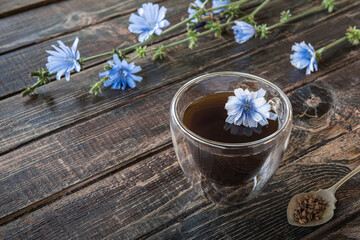 Chicory drink in thermo glass cup with instant granules in spoon on wooden table