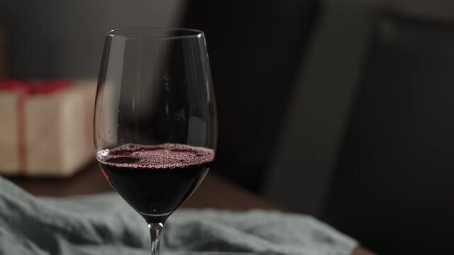 Slow motion red wine into wineglass with gift box on background