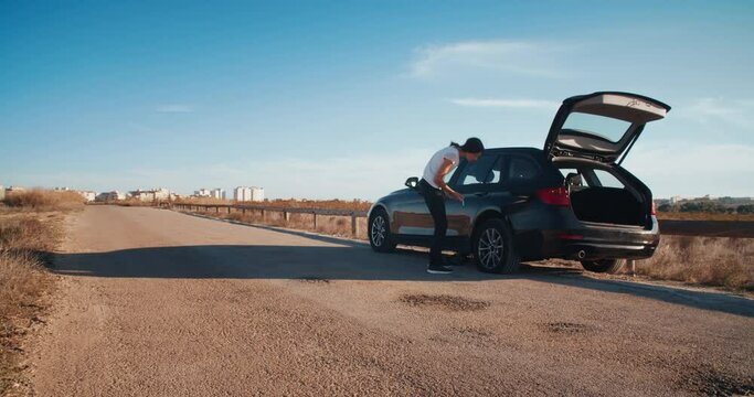 Young attractive woman during travel has vehicle breakdown flat tire and unsuccessfully tries to fix it. Concept of broken car on country road in Spain