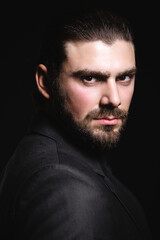 Fototapeta premium Business portrait of a white caucasian man in a black classic suit on a black background. Bearded man looks confident eyes.
