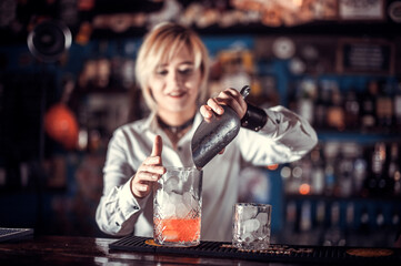 Portrait of girl barman places the finishing touches on a drink in the bar