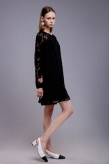 Fashion model in black lace dress, beautiful young woman. Studio shot. Gray background. 