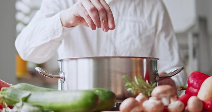 the chef adds spices and salt to the cooking dish in a metal saucepan.