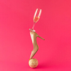 Creative composition made of Christmas bauble, high heels and glass of champagne against pink background. Stylish New Year sparkle eve celebration concept.