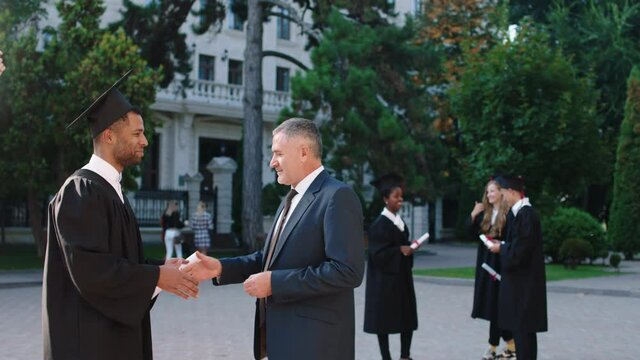 Graduation day in the college garden black guy take his diploma from his college professor very excited they congratulated each other. 4k