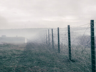 Rows of barbed wire on the state border. The separation of the two countries. Foggy autumn landscape 
