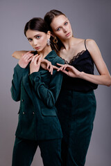 Two fashion models in green suit and black top, green (emerald scarab) skirt, beautiful young women. Studio shot. Gray background. 