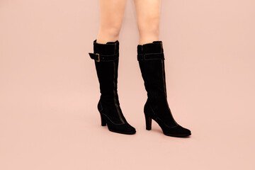 Beautiful Caucasian sexy woman legs in black suede slim high stiletto heels boots on light pink...