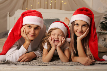 a young family with a little daughter in Santa Claus hats are lying on the bed at home Christmas