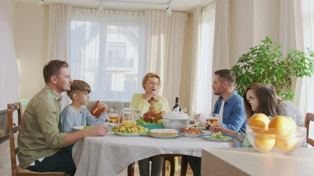 Waist up portrait view of the multi generation family sitting at the dining table during festive dinner, feeling happy, drinking wine and talking