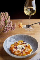 baked pumpkin in ceramic plate on wooden table with glass of white wine. pumpkin with stracciatella and microgreen