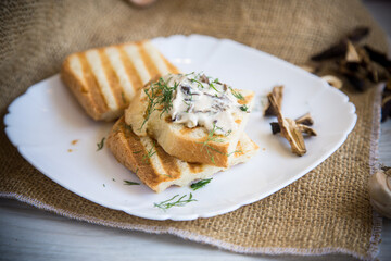 fried bread toast with cheese spread with boiled dried mushrooms on a wooden table.