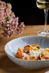 baked pumpkin in ceramic plate on wooden table with glass of white wine. pumpkin with stracciatella and microgreen